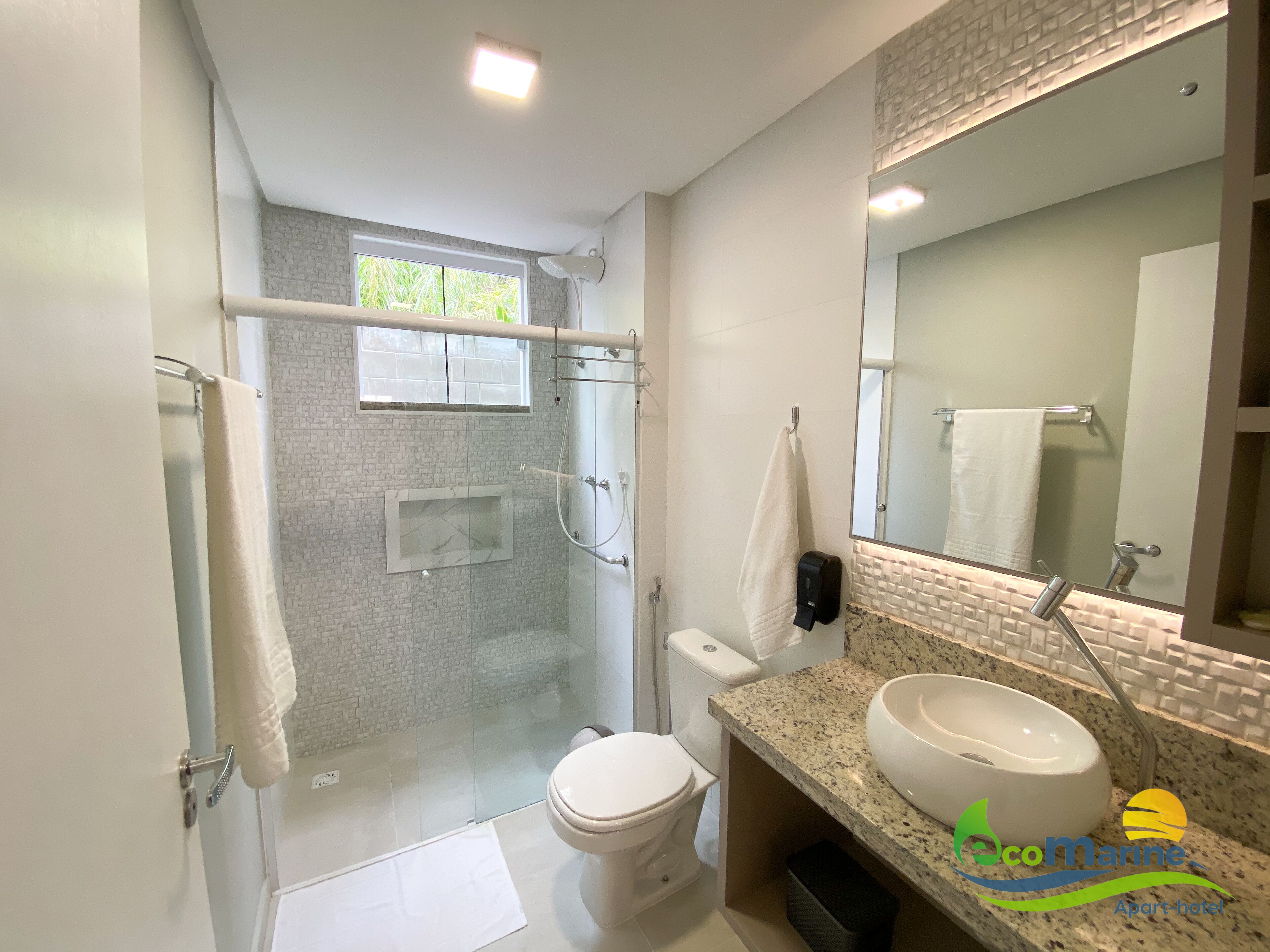 Un baño moderno con cabina de ducha de vidrio, inodoro, lavamanos con un espejo grande y un perchero para toallas.