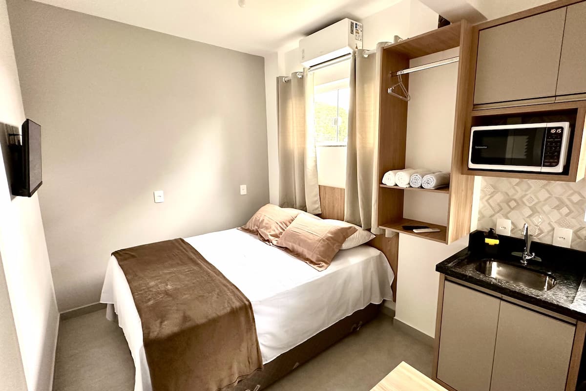 Ein kompaktes Hotelzimmer mit Bett, einer kleinen Küchenzeile, einer Mikrowelle und einem Fenster mit Vorhängen.