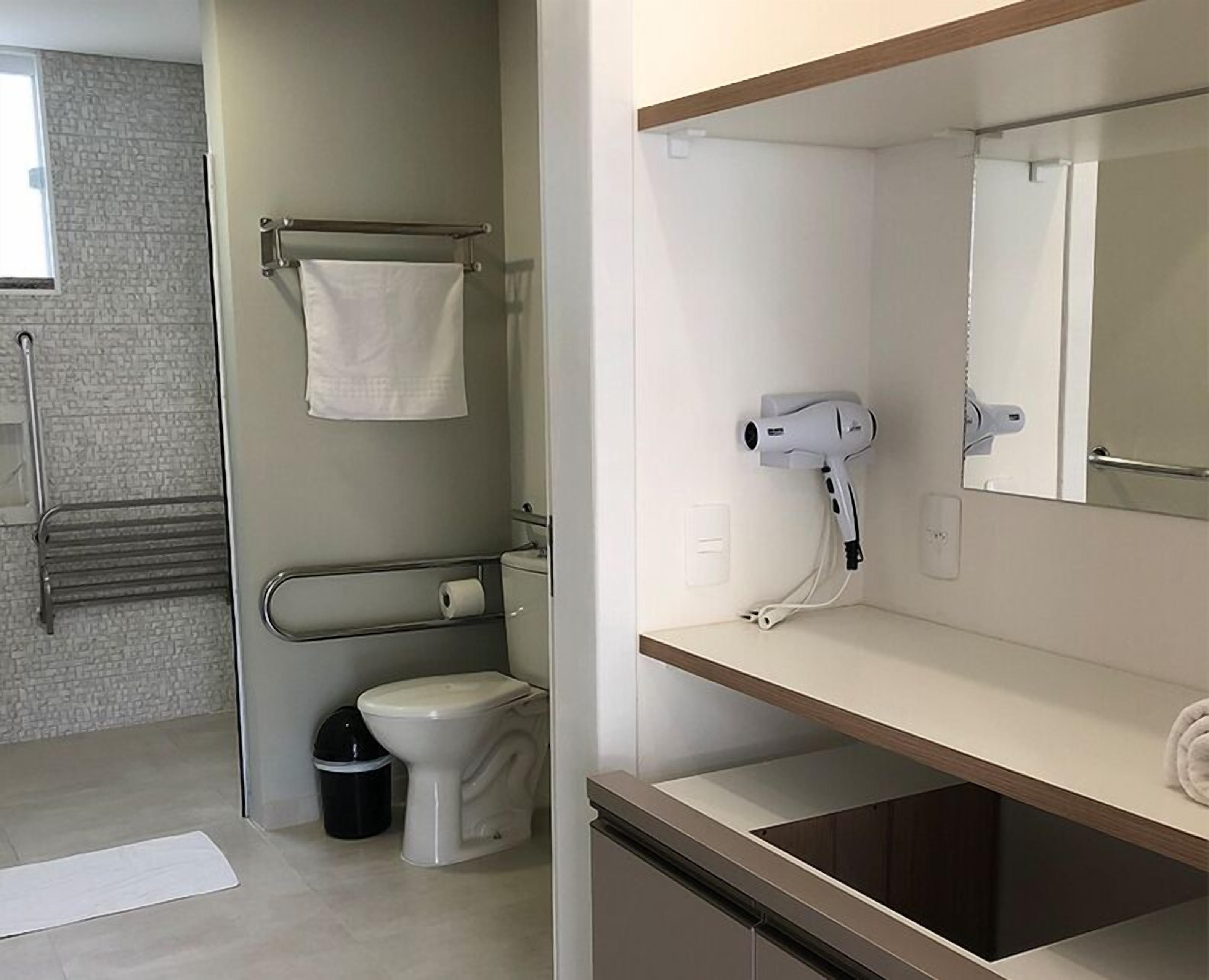 Un baño moderno con inodoro, toallero, secador de pelo y espejo.