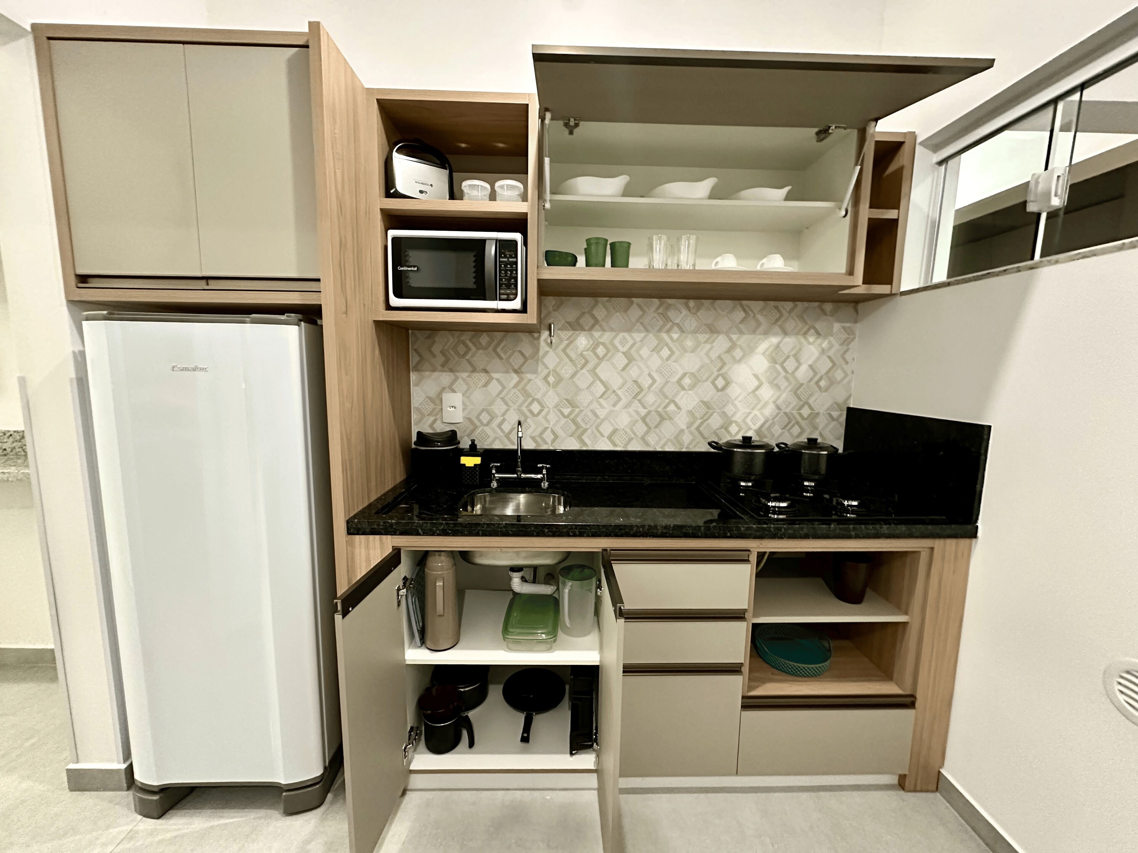 A compact kitchen with a refrigerator, microwave, sink, and various utensils.