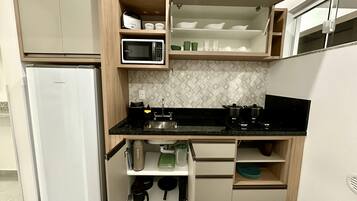 A compact kitchen with a refrigerator, microwave, sink, and various utensils.