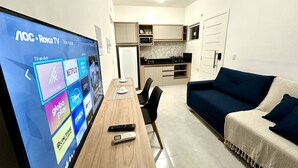 Una sala de estar moderna con una televisión mostrando servicios de streaming, una mesa de comedor con sillas, un sofá y una cocina al fondo.