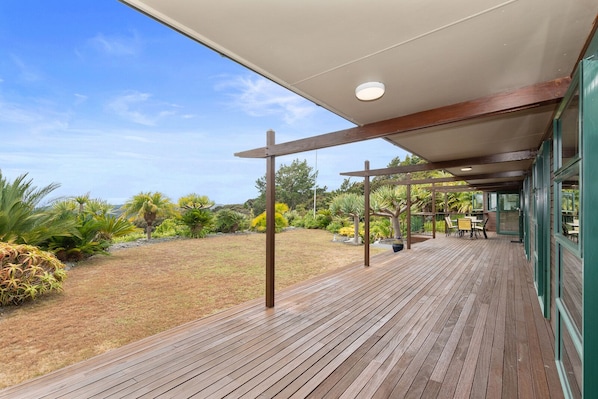 A wooden deck with a covered area, outdoor seating, and a view of a landscaped garden.