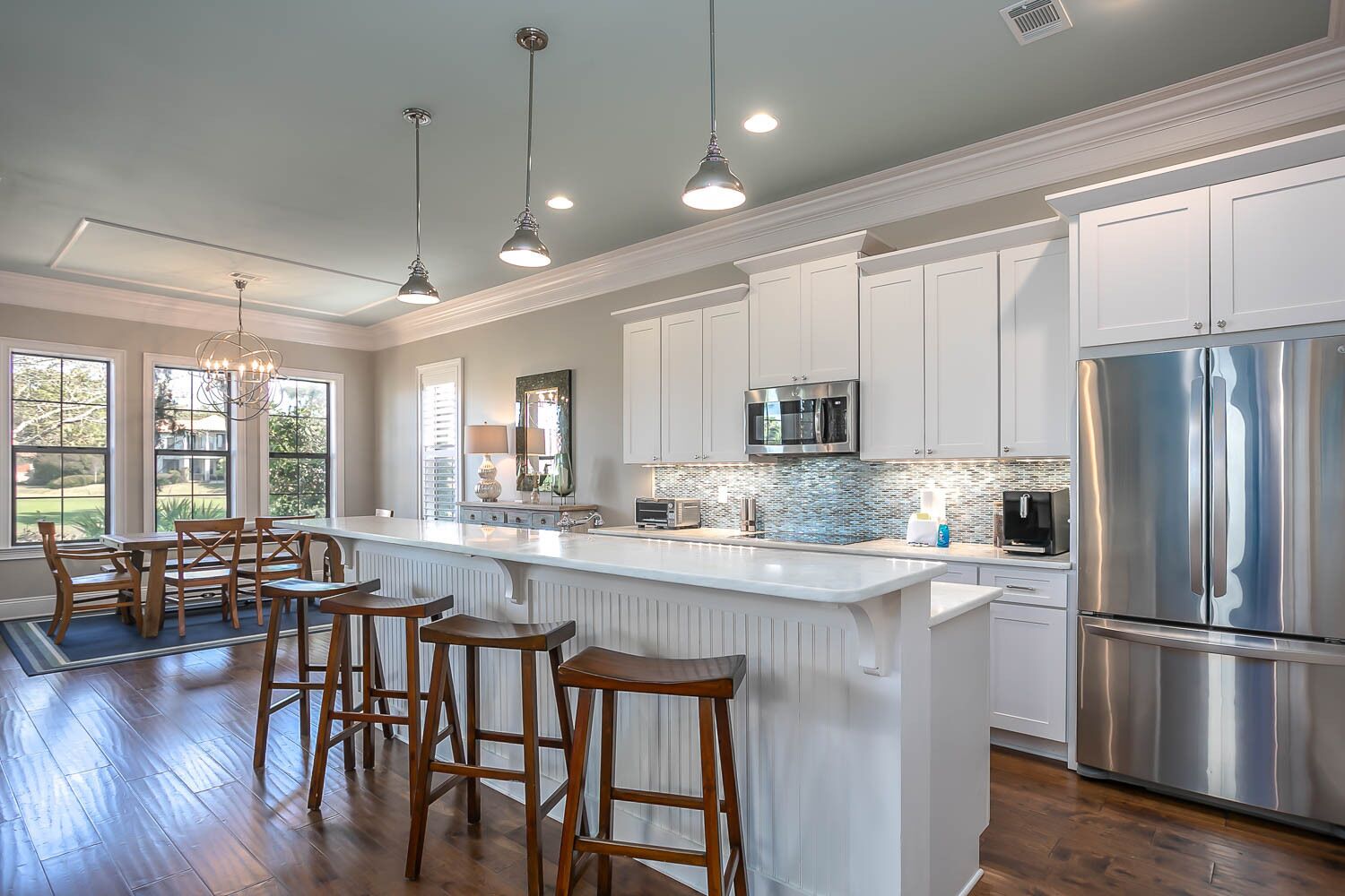 A modern kitchen with white cabinetry, stainless steel appliances, and a central island with bar stools.