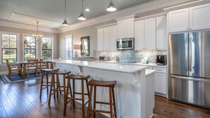 A modern kitchen with white cabinetry, stainless steel appliances, and a central island with bar stools. - Beach,Tons of entertainment, bikes, 2  golf carts, Golf, Amazing Gym, and Marina (Miramar Beach)