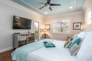 A bedroom with a bed, a TV, a ceiling fan, a dresser, and a window with blinds.