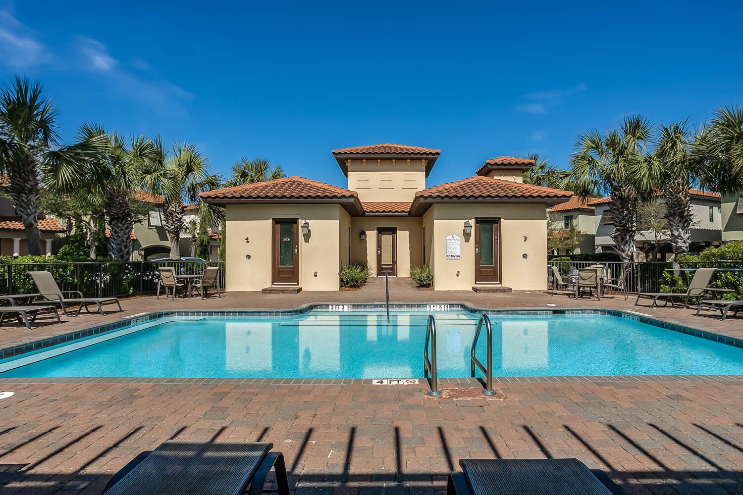 A swimming pool with a clear blue water, surrounded by lounge chairs and palm trees.