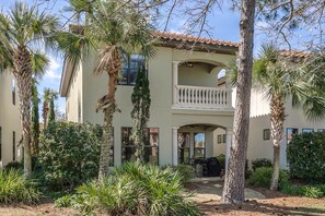 A two-story building with a balcony, surrounded by palm trees and other greenery.