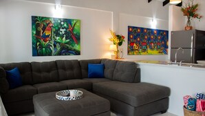 A living room with a grey sectional sofa, a coffee table, and two paintings on the wall. - JJEM Cabanas (Placencia)