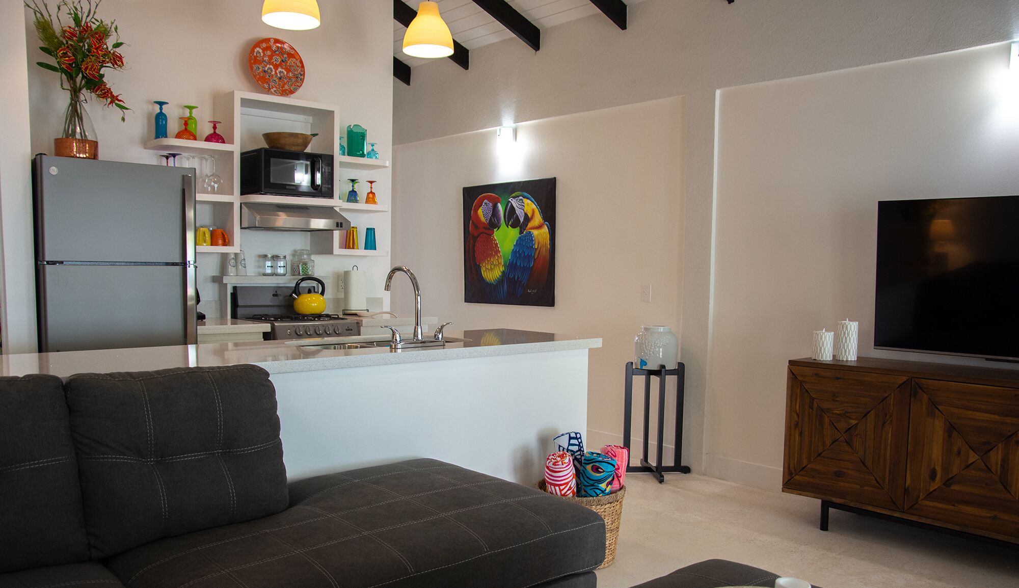 A modern living room with a sofa, a TV, and a kitchen area with a microwave and kettle.