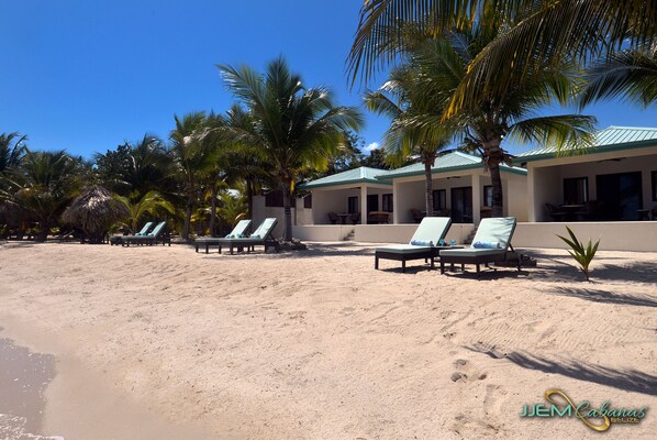 A beachside hotel with lounge chairs and palm trees. - JJEM Cabanas (Placencia)