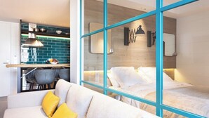 A modern hotel room with a sofa, a bed, and a view through a glass wall to a kitchen area. - Home2Book Lovely Apartment in Santa Cruz (Santa Cruz de Tenerife)