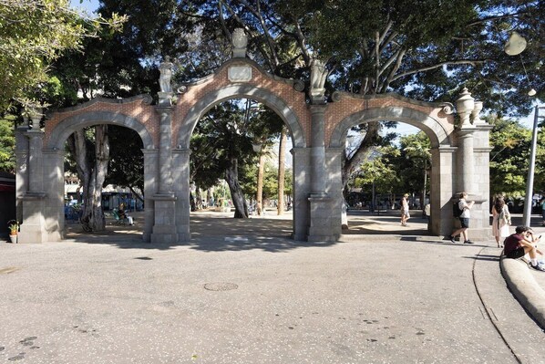 An outdoor stone archway with classical design elements, surrounded by trees and a paved area.