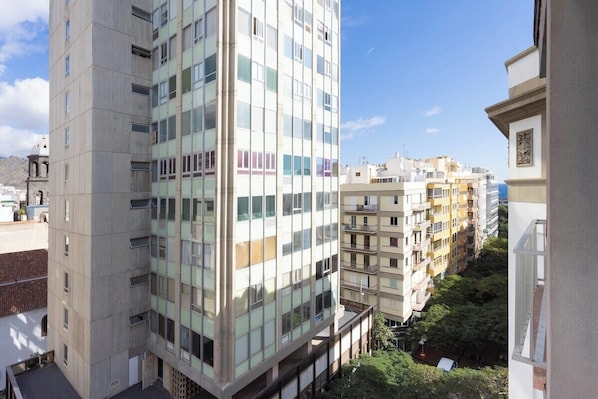 Un edificio residencial de varios pisos con balcones, cielo despejado y vegetación circundante.