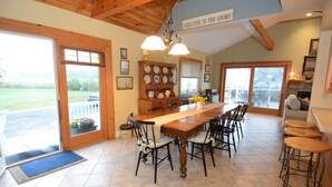 A spacious dining area with a wooden table and chairs, a built-in shelf with dishes, and a view of the outdoors through large sliding doors. - Cozy, year round beach cottage just steps to the water (East Haven)