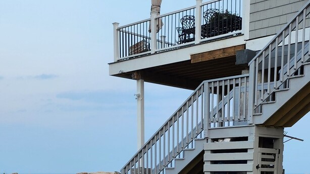 A two-story building with a balcony, outdoor seating, and a staircase. - Cozy, year round beach cottage just steps to the water (East Haven)