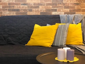 A dark grey sofa with yellow and grey striped pillows, a round table with candles, and a brick wall in the background.