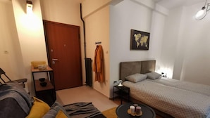 A bedroom with a bed, a sofa, a small table, a coat rack, and a world map on the wall. - Charming 1-bed Apartment Located in Athina (Athens)