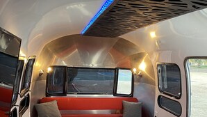 A compact interior with a red sofa, a small table with a plant, and a kitchenette area. - Chic Airstream on a 1 acre lot on the golf course in Scottsdale (Scottsdale)