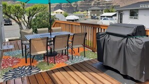 Een terras met een tafel, stoelen, een overdekte barbecue en een kleurrijk kleed.