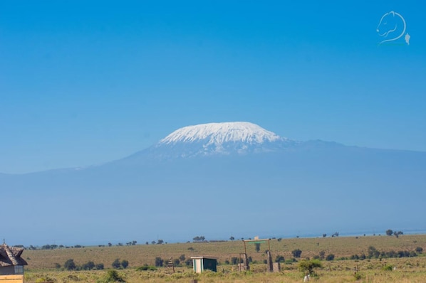 A mountain with a snow-capped peak, a small building, and a clear blue sky.