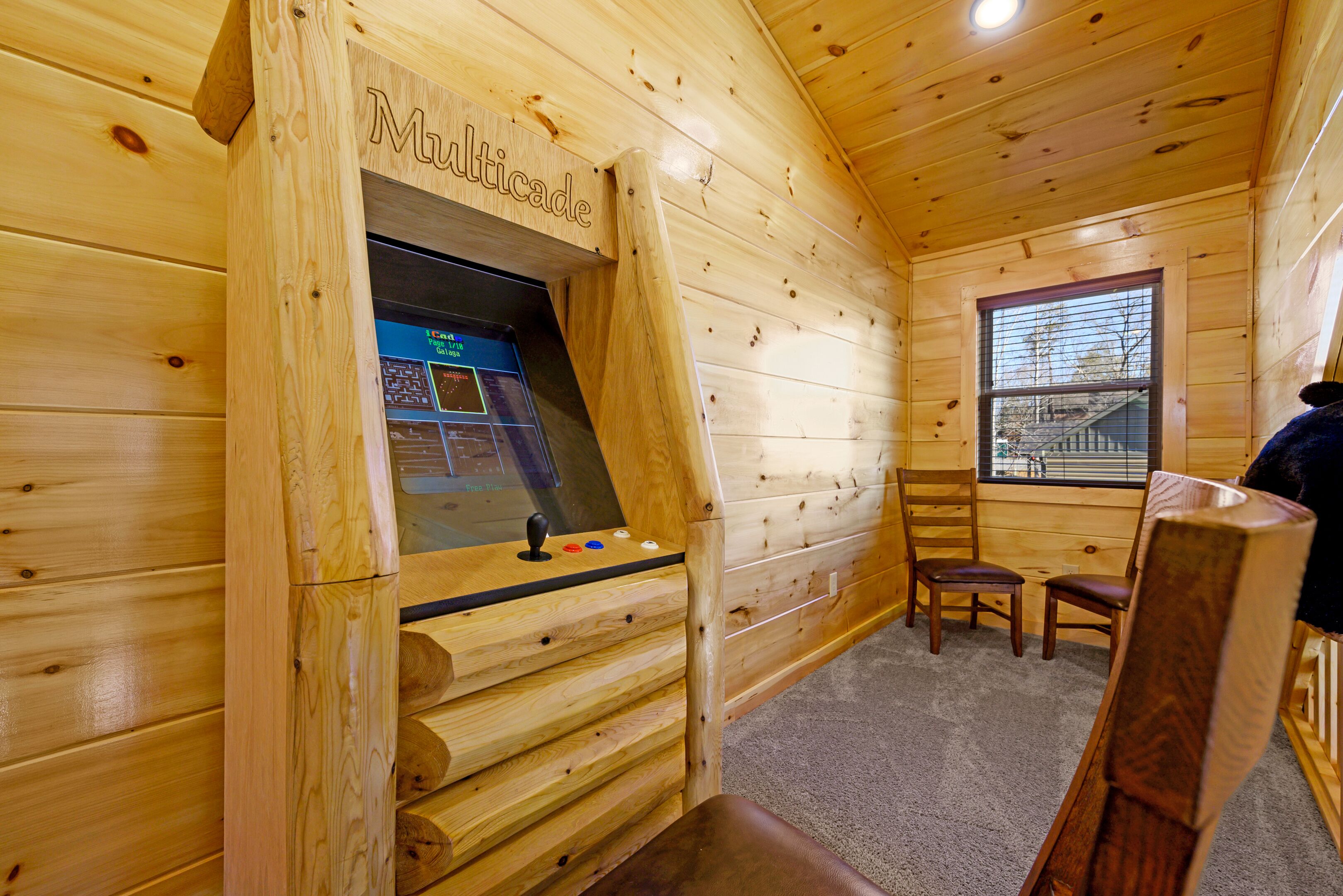 Interior de una cabaña de madera con una zona de juegos de madera que dice 'Multicade', una ventana y dos sillas.