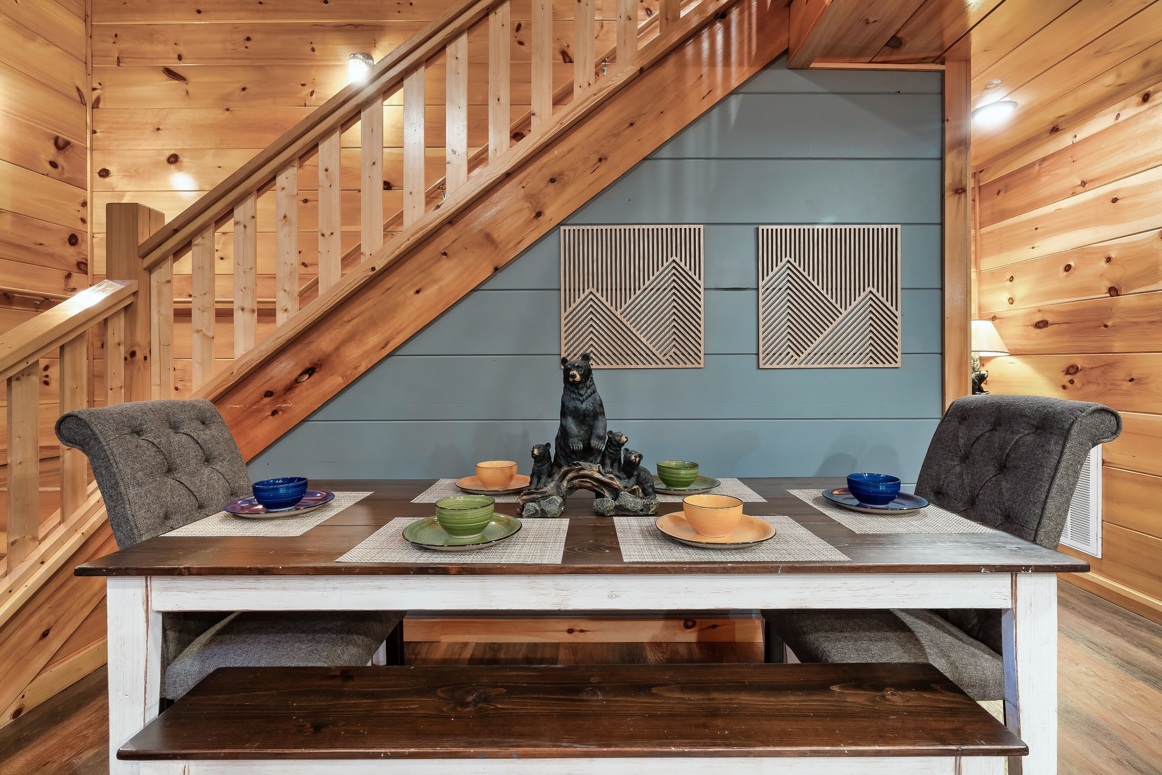A wooden staircase leading to a dining area with a table set for four, surrounded by grey upholstered chairs.