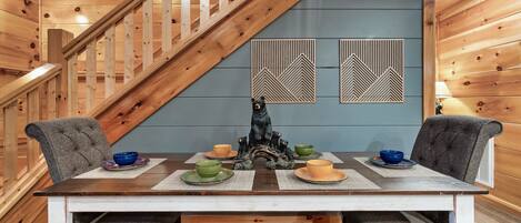 A wooden staircase leading to a dining area with a table set for four, surrounded by grey upholstered chairs.