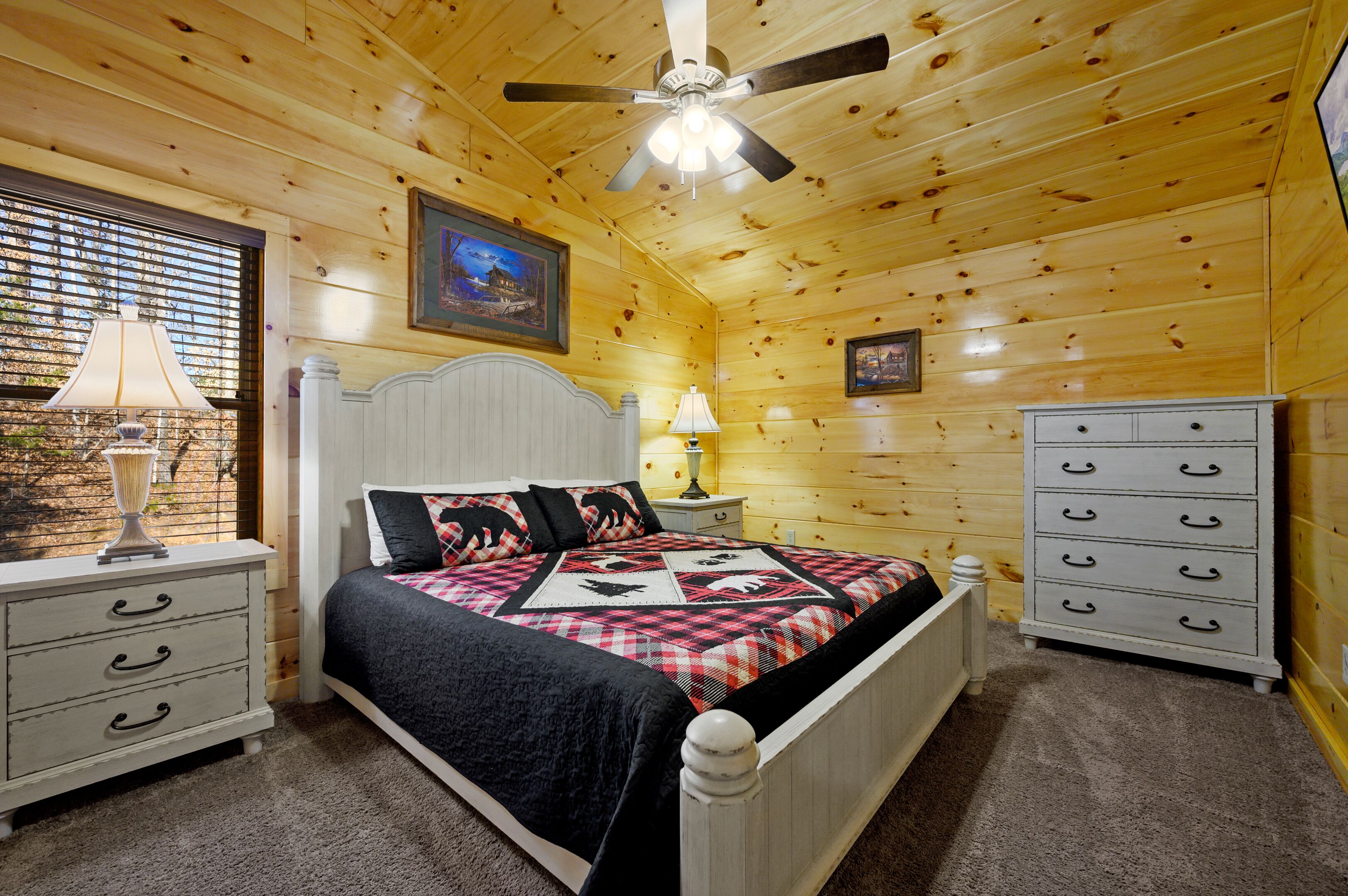 A wooden cabin bedroom with a bed, nightstands, a dresser, and a ceiling fan.