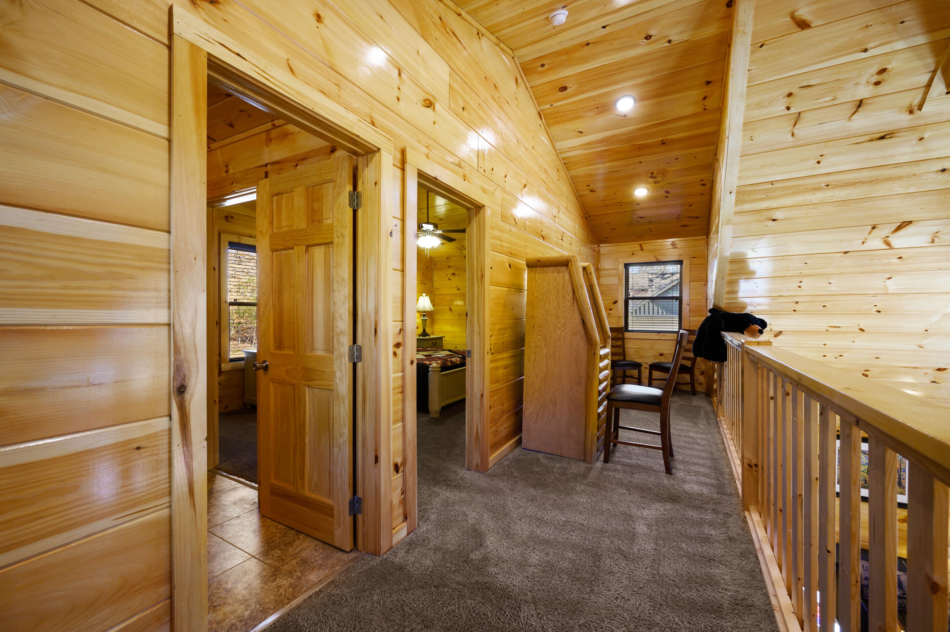 A wooden cabin interior with a high ceiling, a dining area with a table and chairs, and a view through a window.
