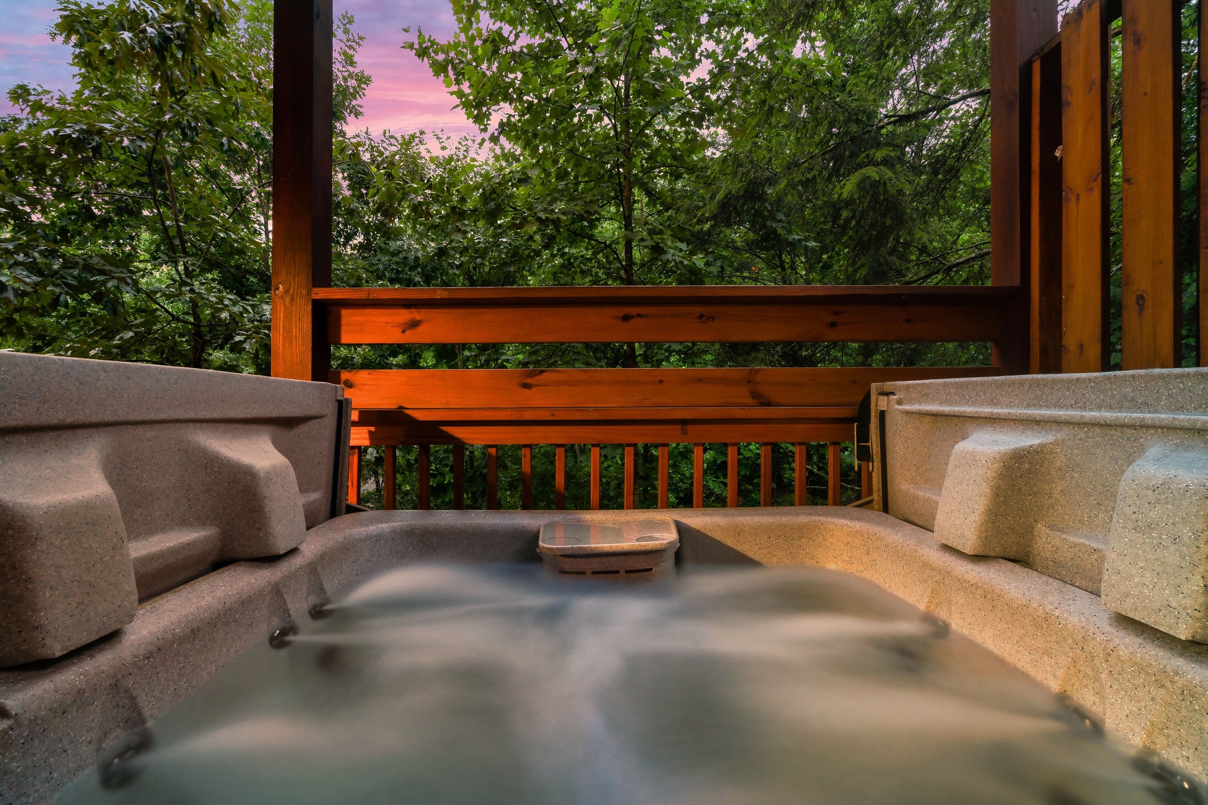 A hot tub with a wooden bench and stone steps, surrounded by trees.