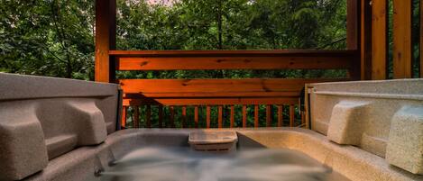 A hot tub with a wooden bench and stone steps, surrounded by trees.
