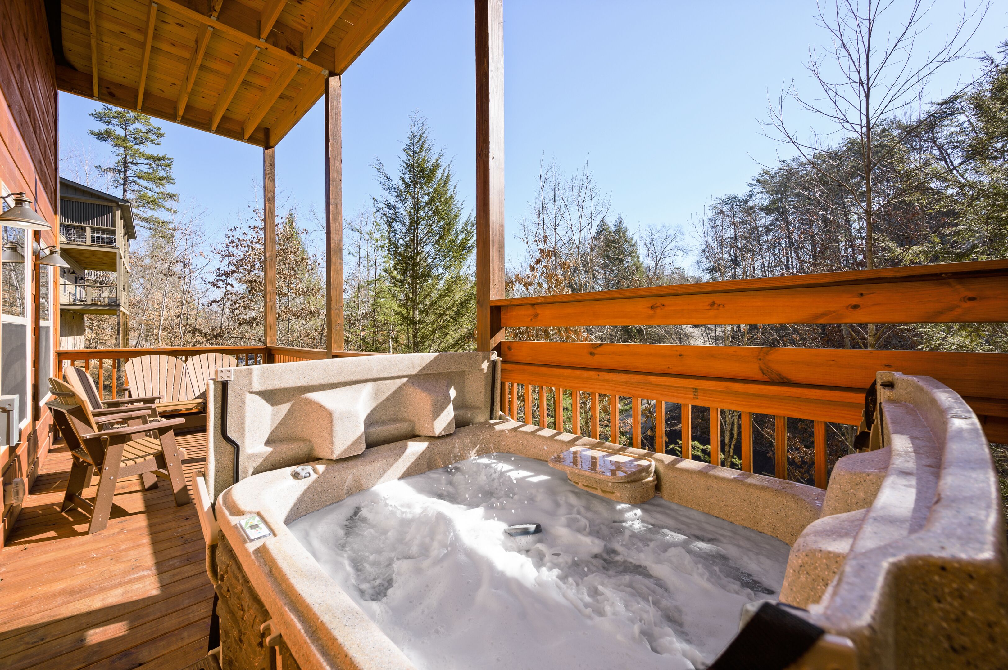 Una terraza de madera con un jacuzzi, sillas y barandilla de madera.