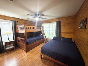 Een kamer met houten lambrisering, stapelbedden, een bureau en een plafondventilator.