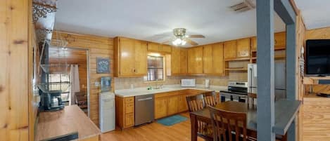 A compact kitchen with wooden cabinets, a dining table, and a ceiling fan.