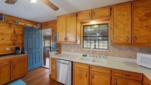 Una cocina con armarios de madera, lavavajillas, ventana y ventilador de techo.