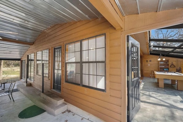 A wooden cabin with large windows, a pool table, and a covered patio area.