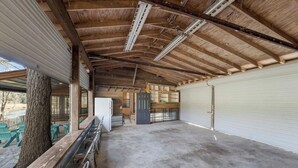 Un espacio amplio cubierto, con piso de concreto, vigas de madera y una gran puerta de garaje blanca.