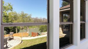 Uitzicht door een raam op een achtertuin met houten omheining, een vijver en een terras met tuinmeubilair.