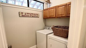 Un lavadero con un letrero que dice "LAUNDRY" en la pared, una lavadora, una secadora y una cesta de mimbre sobre la secadora.
