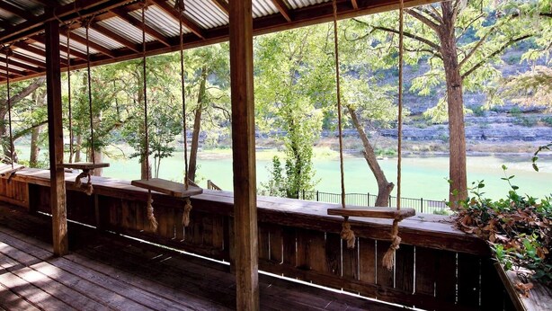 Una terraza de madera cubierta con bancos, con vista a un cuerpo de agua tranquilo y árboles.