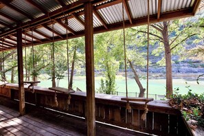 A covered wooden deck with benches overlooking a calm body of water and trees.