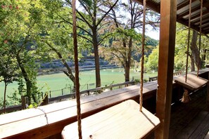 A wooden deck with benches overlooking a river and forested hills. - Tiki Loft #1 | Guadalupe | River Road | Sleeps 4 (New Braunfels)