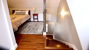 Une chambre à coucher avec un lit, une petite table, une lampe et un escalier menant à une autre pièce.