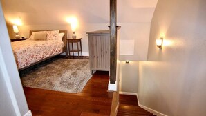 Un dormitorio con cama, mesita de noche, silla, aparador de madera y una escalera.