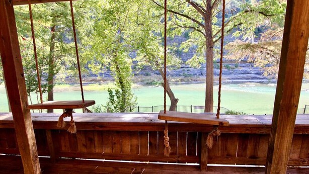 Una terraza de madera con dos bancos da vistas a un paisaje natural con árboles y un cuerpo de agua.
