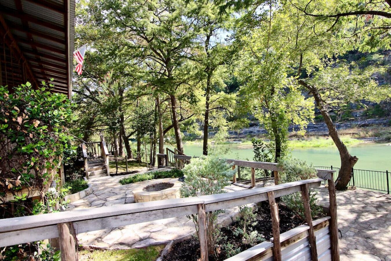 A stone pathway leading to a wooden deck with a fire pit, surrounded by trees and overlooking a body of water.