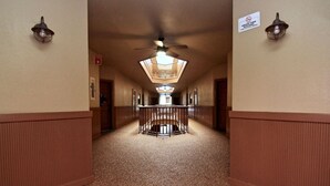 Un pasillo de hotel con una escalera central, un ventilador de techo y un cartel que indica que es un edificio libre de humo.