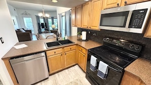 Una cocina moderna con armarios de madera, lavavajillas de acero inoxidable, estufa negra y microondas.