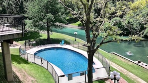 Una piscina con borde curvo, rodeada por una valla metálica y una banca cerca.